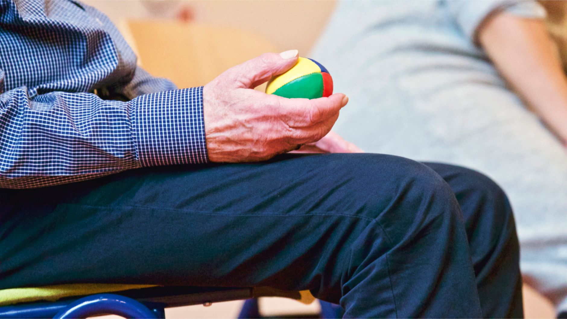 Ältere Person trainiert die Handfunktion mit einem bunten Therapieball
