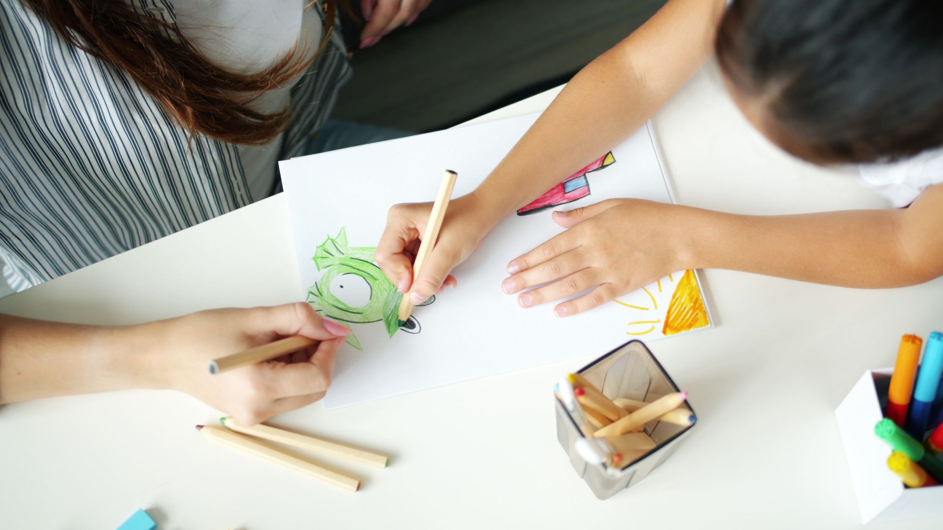 Kind und Erwachsene malen gemeinsam ein buntes Bild am Tisch